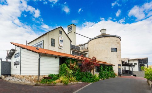 A rustic building with a round silo, surrounded by greenery and under a blue sky with clouds.