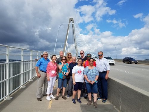 A group of people poses on a bridge with a cloudy sky in the background.