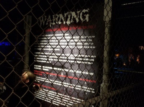 A warning sign on a fence, detailing safety instructions and precautions, with a person partially visible in the foreground.