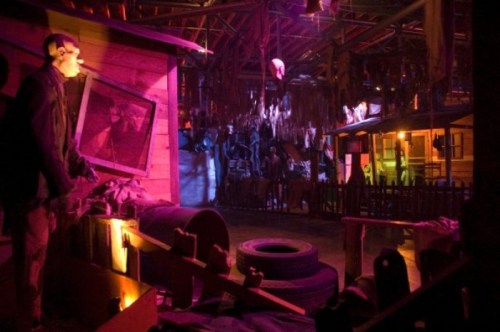 A dimly lit haunted scene with eerie decorations, including a mannequin and hanging props, creating a spooky atmosphere.