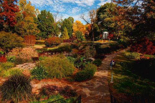 A vibrant garden in autumn, featuring colorful foliage, winding paths, and a gazebo under a blue sky.