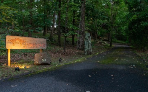 A wooden sign reading "Stoneflower" beside a dark, winding path through a lush, green forest.
