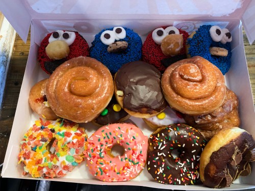 A box of colorful donuts, including frosted, sprinkled, and character-themed designs, arranged neatly.
