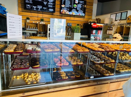 A display case filled with various pastries and donuts, with a menu board in the background.