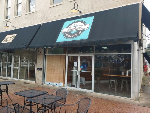 Exterior of Babe's Doughnut Co. with a blue sign, open door, and outdoor seating area on a brick sidewalk.