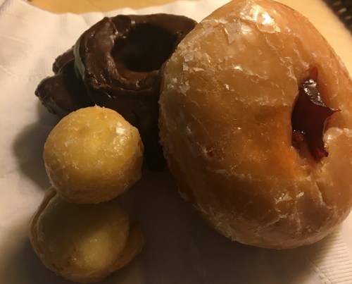 A plate with a glazed donut, a chocolate-covered donut, and two small cream-filled pastries.