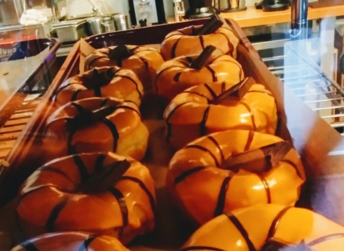 A display of glazed pumpkin-shaped pastries with chocolate stripes, arranged in a wooden tray.