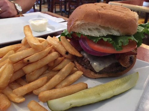 A juicy burger with lettuce, tomato, onion, and cheese, served with crispy fries and a pickle on the side.