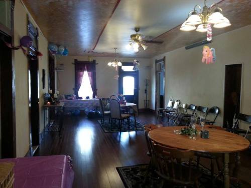 A spacious room with wooden floors, tables, chairs, and decorations for a celebration, featuring balloons and a cozy atmosphere.
