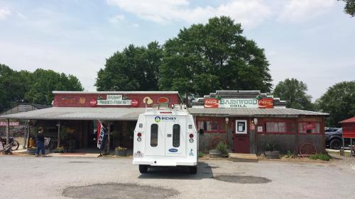 A rustic roadside market and grill with a vintage truck parked in front, surrounded by trees and a clear sky.