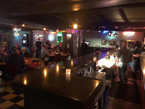 A cozy bar scene with patrons enjoying drinks and food, dim lighting, and a lively atmosphere.