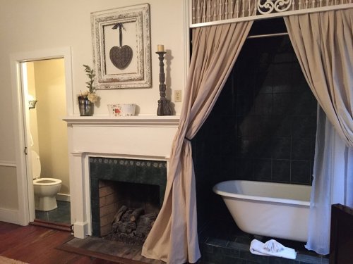 A cozy bathroom featuring a freestanding tub, a fireplace, and a curtain separating it from a small toilet area.