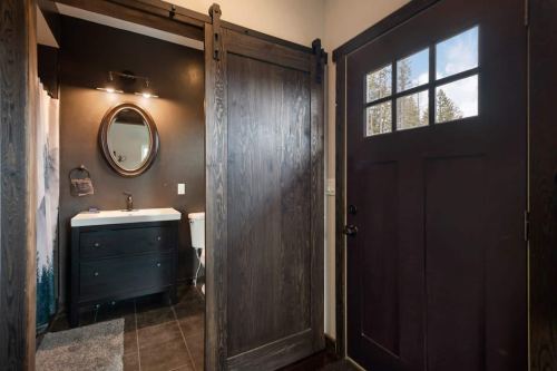 A modern bathroom with dark wood accents, a round mirror, and a door leading outside.