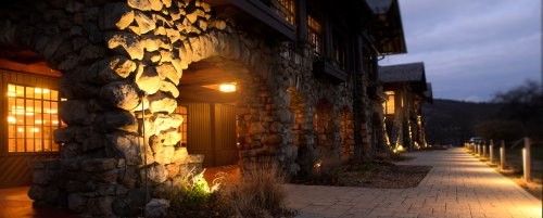 A stone building with warm lights glowing from windows, set along a paved pathway at dusk.