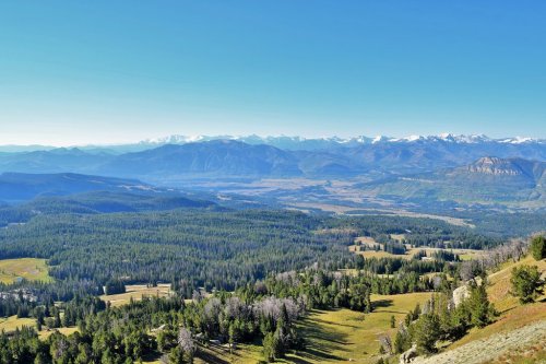 A panoramic view of lush green valleys and distant snow-capped mountains under a clear blue sky.