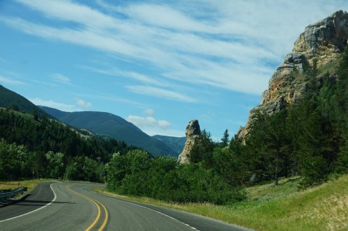A winding road surrounded by lush greenery and rocky cliffs under a blue sky with scattered clouds.