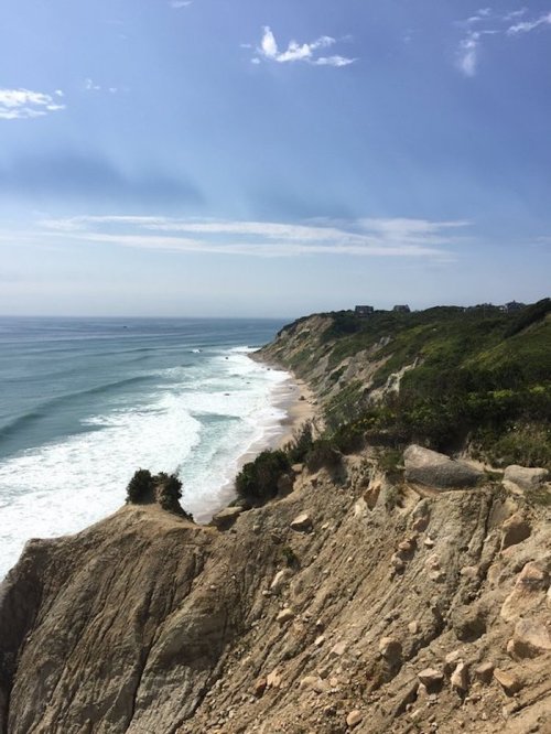 A scenic coastal view with cliffs, sandy beach, and gentle waves under a clear blue sky.