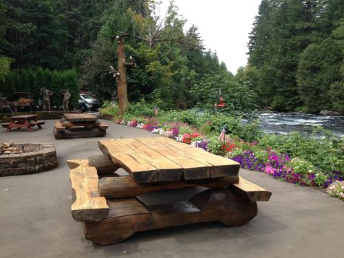 A rustic wooden picnic table by a river, surrounded by colorful flowers and lush greenery.