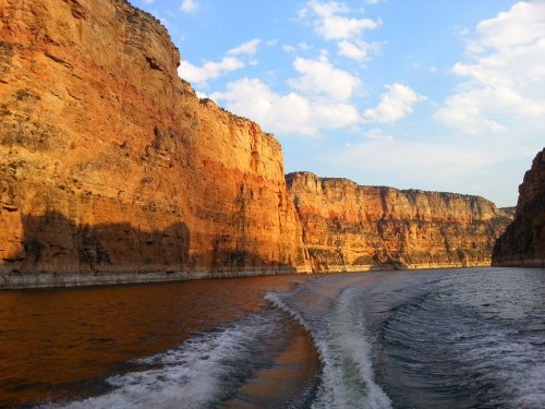 A scenic view of rocky cliffs beside a calm waterway, with a blue sky and scattered clouds above.
