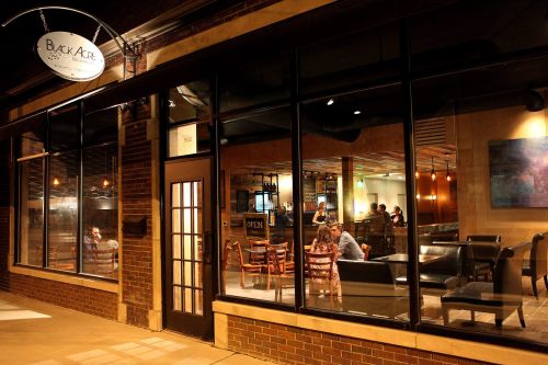 A cozy café exterior at night, featuring large windows, warm lighting, and patrons enjoying their time inside.