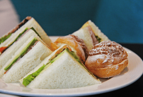 A plate with triangular sandwiches filled with vegetables and meats, alongside a small pastry dusted with powdered sugar.