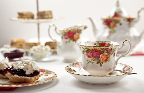 A floral tea set with a cup, saucer, and plate of scones topped with jam and cream, elegantly arranged on a table.