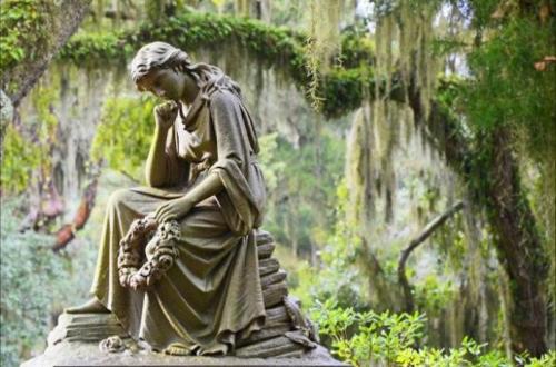A serene statue of a woman sitting thoughtfully, surrounded by lush greenery and hanging moss.