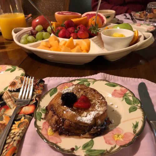 A plate with a slice of French toast topped with berries, alongside a colorful fruit platter and a glass of juice.