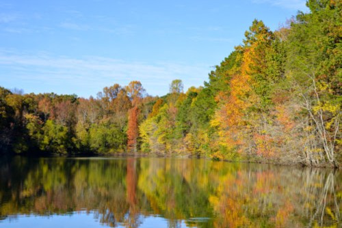 A serene lake surrounded by vibrant autumn foliage reflecting on the water under a clear blue sky.