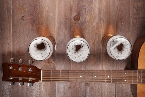 Three glasses of beer with foam sit on a wooden table next to an acoustic guitar.