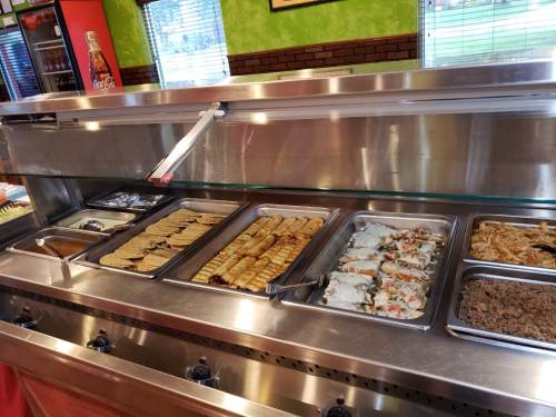 A buffet display featuring various Mexican dishes, including tortillas, enchiladas, and a meat dish, in a stainless steel tray.