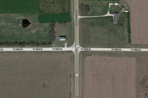 Aerial view of an intersection in a rural area, surrounded by fields and a few buildings.