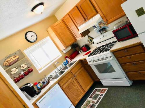 Cozy kitchen with wooden cabinets, a gas stove, sink, and various appliances, featuring a clock and decorative wall art.