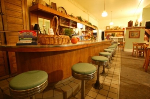 A cozy diner interior featuring a wooden counter with green stools and shelves filled with vintage items.
