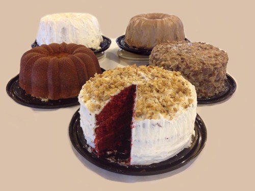 A variety of cakes on black plates, including a red velvet cake with a slice cut out and three bundt cakes in the background.