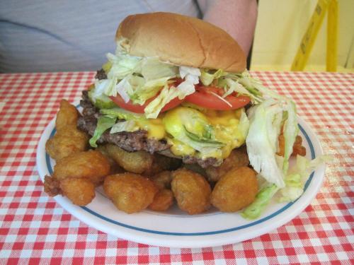 A large cheeseburger topped with lettuce and tomato, served with a side of golden fried bites on a checkered tablecloth.