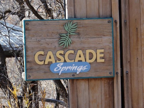 Wooden sign reading "Cascade Springs" with a leaf design, surrounded by trees and natural scenery.