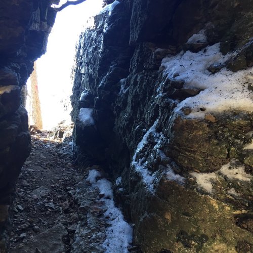 Narrow rocky passageway with snow and sunlight at the end, surrounded by rugged stone walls.