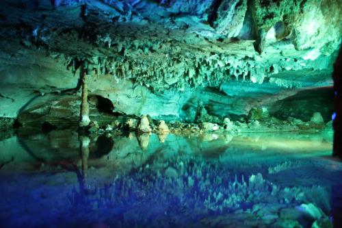 A colorful cave interior with stalactites and stalagmites reflected in still water.