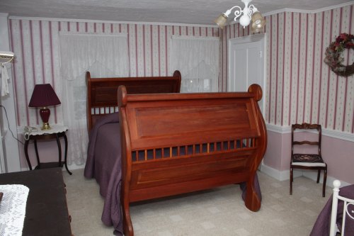 A cozy bedroom featuring a wooden sleigh bed, striped wallpaper, and a vintage lamp on a side table.
