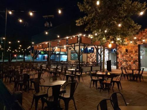 Outdoor dining area at night, featuring string lights, empty tables, and a colorful wall mural.