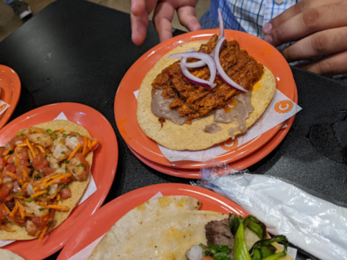 A close-up of a taco with shredded meat and onions on a plate, alongside other dishes on a table.