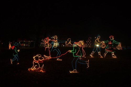 Colorful holiday lights depict people and a dog enjoying a festive outdoor scene at night.