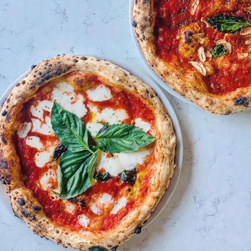 Two pizzas on white plates: one with mozzarella and basil, the other with a rich tomato sauce and garlic.