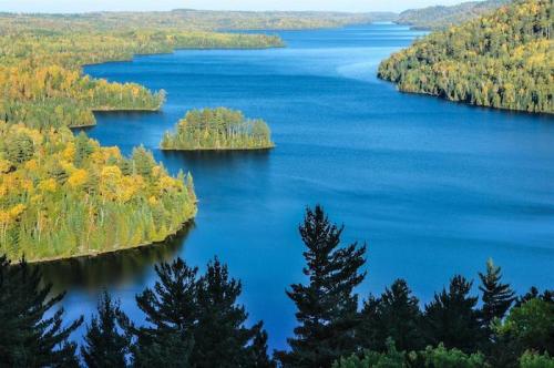 A serene lake surrounded by lush green and autumn-colored trees, with small islands dotting the water's surface.