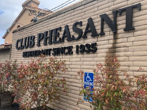 Sign for Club Pheasant restaurant, established in 1935, with nearby parking sign and greenery.