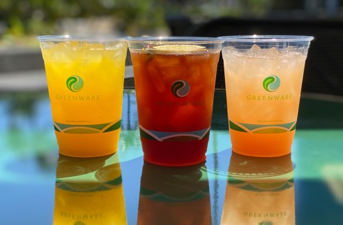 Three colorful drinks in clear cups with the "Greenware" logo, sitting on a reflective surface.