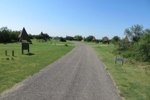 A winding gravel path through a grassy area with triangular structures and trees under a clear blue sky.