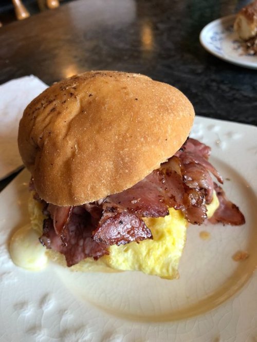 A sandwich with a soft bun, filled with layers of bacon and a fluffy egg patty, served on a white plate.