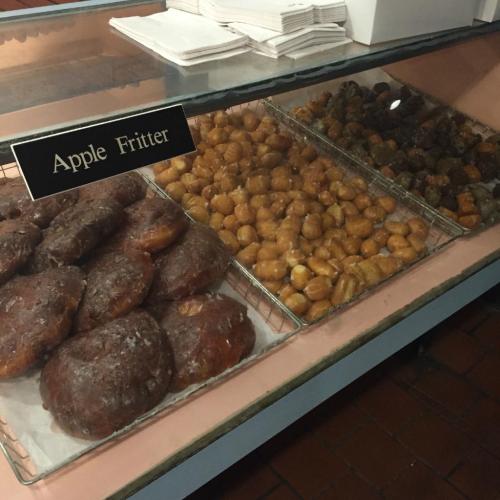 A display case filled with various types of donuts, including apple fritters and small glazed donuts.